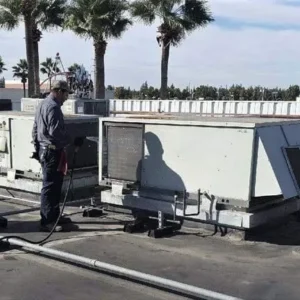 A technician stands on a rooftop next to large commercial HVAC units.