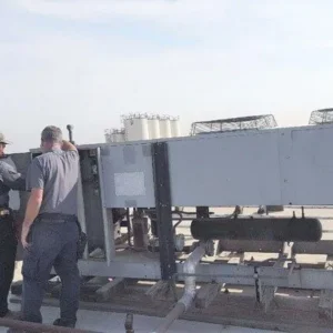 Two technicians work on a large commercial HVAC unit installed on a flat roof.