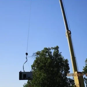 A construction crane lifts a rectangular metal object into the air against a clear blue sky.