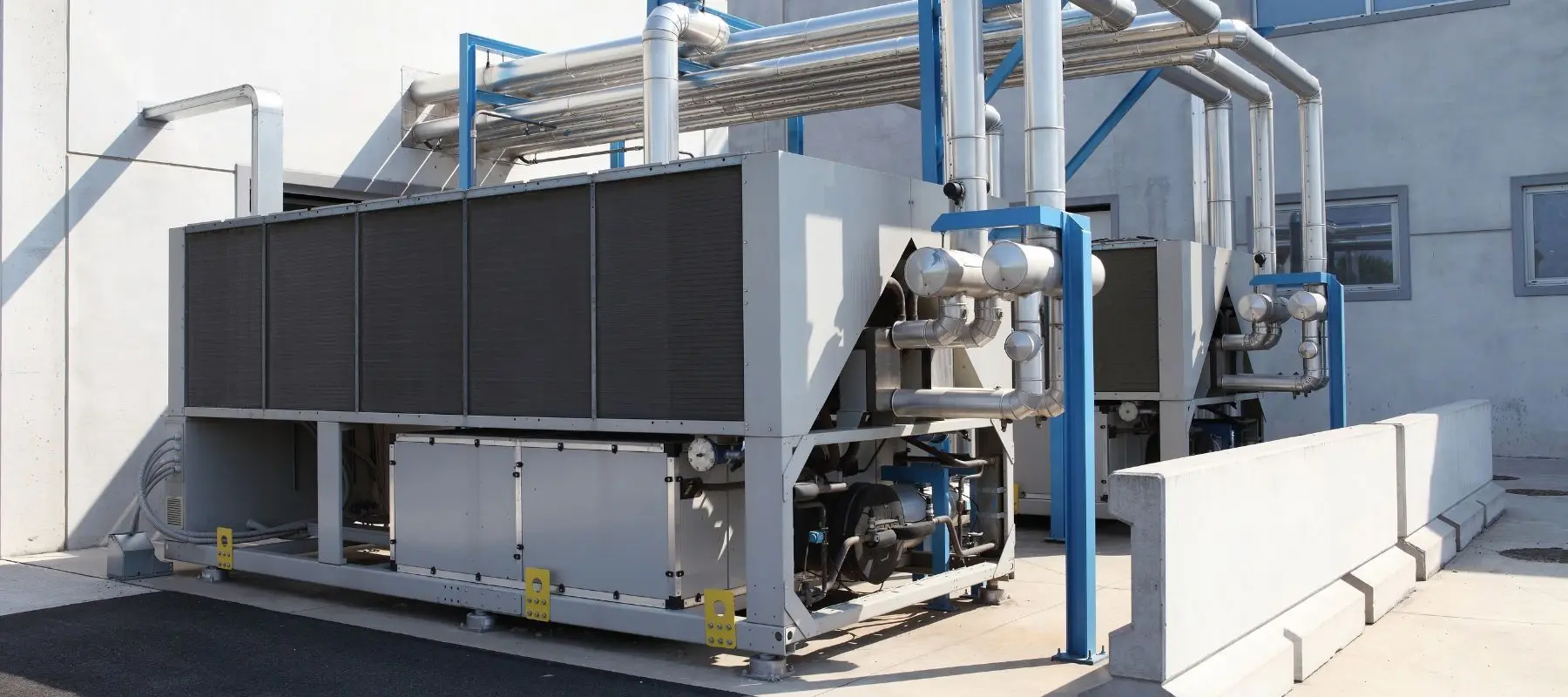 Large industrial chiller units with silver piping installed outside a concrete building.